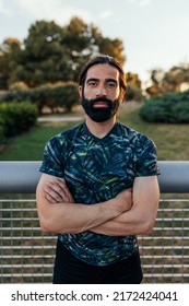 A Strong Caucasian Man Is Standing In The City Park With His Arms Folded