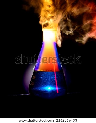 Strong chemical reaction with a lot of smoke and vapors inside Erlenmeyer flask. Ignition is starting. Vessel with a blue liquid is standing on the table. Background picture.