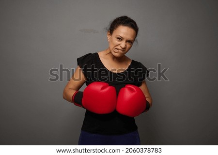 Strong concentrated African woman looks at camera posing against gray wall background with red boxing gloves. Concept of Black Friday and boxing Day, Blow to prices with copy space for advertisement