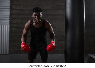 A strong and confident African-American boxer wearing red gloves, showing off his athletic build and determination, he shouts and expresses aggression in the dark, minimalist atmosphere of the gym. - Powered by Shutterstock