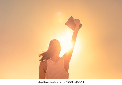 Strong Confident Young Woman Holding Up Book Bible Up Tot He Sky. 