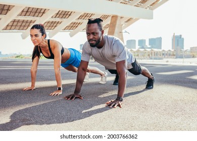 Strong couple doing pushups outdoors. Beautiful woman exercising with her attractive personal trainer.