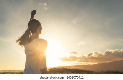Strong, determined, confident woman with her fist up in the air facing sunset.