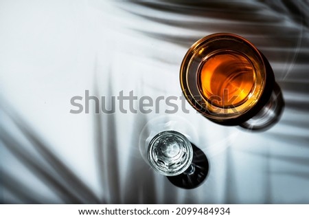 Strong drinks in glasses: cognac and vodka. White background with hard light and harsh shadows