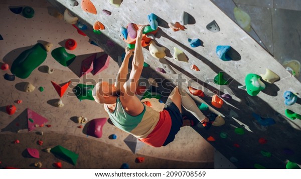 Strong Experienced Rock Climber Practicing Solo\
Climbing on Bouldering Wall in Gym. Man Exercising at Indoor\
Fitness Facility, Doing Extreme Sport for His Healthy Training.\
Lifestyle Portrait.