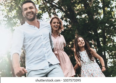 Strong family bonds. Happy young family of three holding hands and smiling while running in park - Powered by Shutterstock