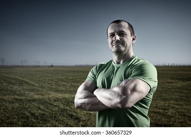 Strong Farmer Man In T-shirt Posing Near A Field Of Rye At Sunset