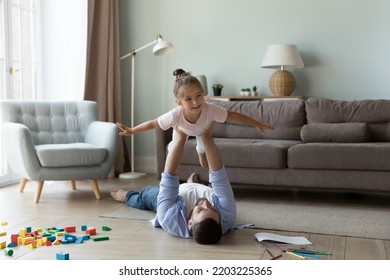 Strong father lifting excited cheerful daughter kid up in air, playing airplane, exercising on heating floor, doing acroyoga support with child, having fun. Fatherhood, family concept - Shutterstock ID 2203225365