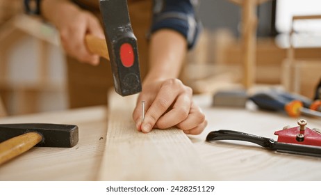 Strong female carpenter's hands drive nail into wood plank at professional carpentry workshop - Powered by Shutterstock