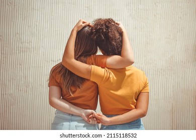 Strong female friendship. Rear view two teen girls best friends holding hands behind back and hugging while standing in front of beige wall outdoors - Shutterstock ID 2115118532