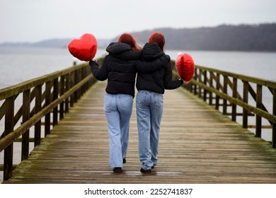                 Strong female friendship. Rear view of two teenage girls best friends holding hands with heart shaped balloons in hands while walking on a bridge outdoors.Selective focus               - Shutterstock ID 2252741837