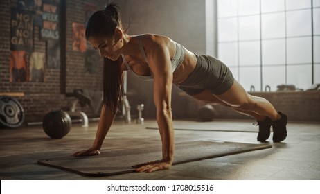 Strong and Fit Athletic Woman in Sport Top and Shorts is Doing Push Up Exercises in a Loft Style Industrial Gym with Motivational Posters. It's Part of Her  Fitness Training Workout. Warm Light. - Shutterstock ID 1708015516