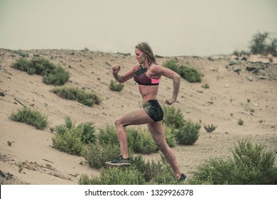 A Strong, Fit Female Athletes Covered In Mud Running Down A Rough Terrain With A Desert Background In An Extreme Sports Race With A Grungy Textured Finish
