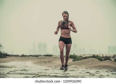 A Strong, Fit Female Athletes Covered In Mud Running Down A Rough Terrain With A Desert Background In An Extreme Sports Race With A Grungy Textured Finish
