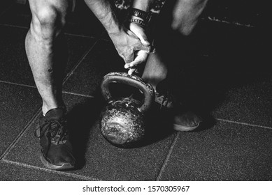 Strong fit muscular man with muscles holding heavy kettlebell with his hand on the gym floor prepared for cross strength and conditioning training and workout black and white - Powered by Shutterstock