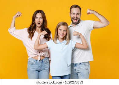 Strong Funny Young Parents Mom Dad With Child Kid Daughter Teen Girl In Basic T-shirts Showing Biceps Muscles Isolated On Yellow Background Studio Portrait. Family Day Parenthood Childhood Concept