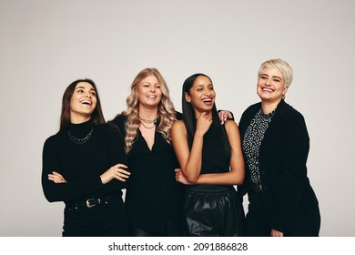 Strong Group Of Women Smiling In A Studio. Four Happy Women Looking Happy While Standing Together Against A Studio Background. Group Of Empowered Women Standing In A Studio.