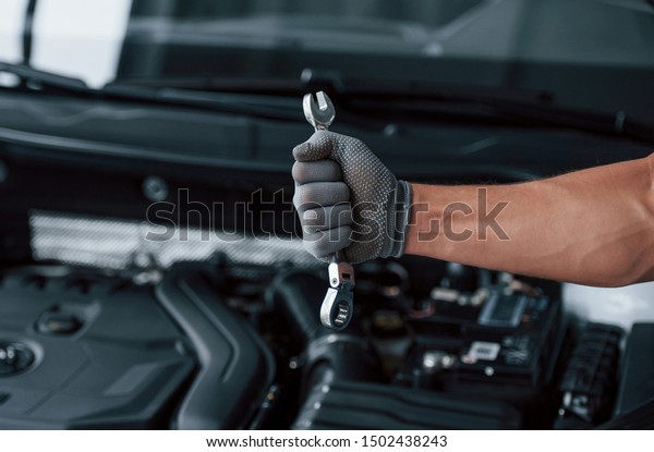 In the strong hand. Holds wrench in front of\
broken automobile.