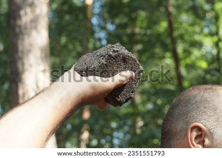 a strong hand of a man holds a large black heavy stone near his head before throwing and attacking during the day on the street