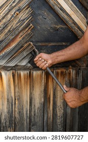 A strong hand wielding a rustic tool on a textured wooden surface, capturing the essence of manual craftsmanship and woodworking skills.