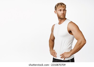 Strong And Handsome Blond Male Athlete, Sportsman In Wireless Earphones Workout In Gym, Looking Around, Listening Music And Exercise, White Background