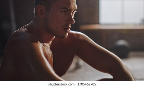 Strong Handsome Fit Shirtless Man Sitting In A Loft Industrial Gym With Motivational Posters. He's Catching His Breath After Intense Fitness Training Workout. Sweat All Over His Body.