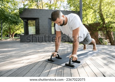 Strong handsome man training with push up bars in summer park