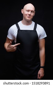 Strong Handsome Smiling Bald Guy Wearing Black Apron Pointing His Finger On His Chest. Butcher, Baker, Chef Or Waiter Concept. Mockup For Restaurants, Grossery Shops, Bakery, Butchery.