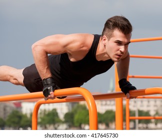 Strong handsome young guy doing bar street workout.