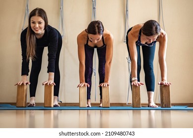 Strong happy athletic female performing ardha uttanasana posture with hands on wooden brick. Sports woman practicing yoga Iyengar with props in group class enjoying harmony balance healthy lifestyle