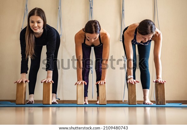 Strong happy athletic female performing ardha\
uttanasana posture with hands on wooden brick. Sports woman\
practicing yoga Iyengar with props in group class enjoying harmony\
balance healthy\
lifestyle