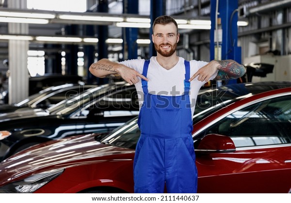Strong happy young male professional technician car\
mechanic man wears denim blue overalls white t-shirt point on\
himself work in light modern vehicle repair shop workshop indoors\
Tattoo traslate fun