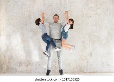 Strong healthy millennial smiling father holding lifting two little adorable kids on hands. Happy family of three having fun, playing, enjoying spending weekend leisure active time together at home.