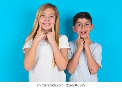 Strong Healthy Straight White Teeth. Close Up Portrait Of Happy Two Kids Boy And Girl Standing Over Blue Background With Beaming Smile Pointing On Perfect Clear White Teeth.