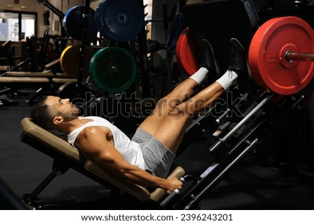 Strong Hispanic man doing leg press at a gym.