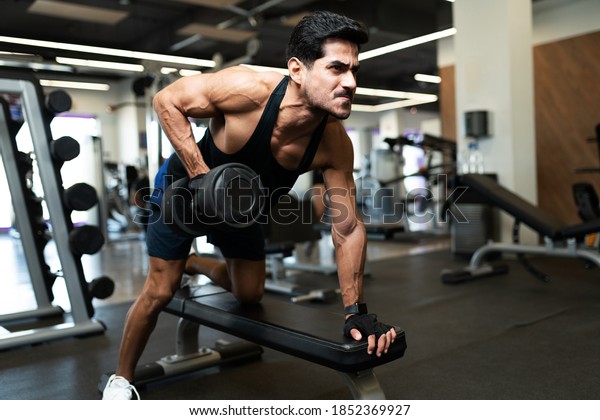 Strong hispanic young man doing a weight\
lifting workout in a bench at the fitness\
club