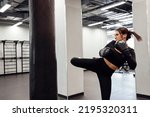 Strong latin boxing woman jump kick to huge punching bag at fitness gym. Athletic girl training Muay Thai boxing for bodybuilding and healthy lifestyle concept. Workout in sport club