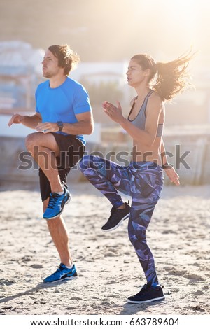 Strong lean couple doing intense high knees exercise on sand, keeping fit healthy lifestyle