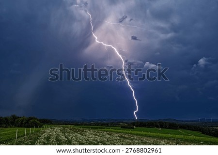 Strong lightning strike during a thunderstorm over an open rural landscape. Dark storm clouds and intense electrical discharge over the countryside in Germany.