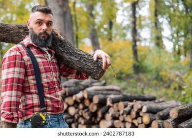 The strong lumberjack carrying a piece of wood on his shoulder towards a pile of chopped logs. - Powered by Shutterstock