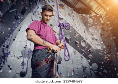 A strong male climber climbs an artificial wall with colorful grips and ropes. - Powered by Shutterstock