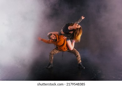 Strong male dancer and an elegant female dancer perform an exotic and unique dance moves in front of a black background while wearing urban clothes. - Powered by Shutterstock