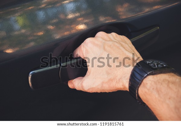 Strong male hand with wrist watch opens\
car door, closeup photo with selective\
focus