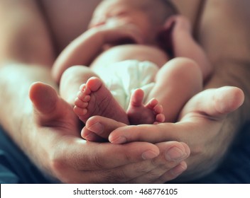 Strong Male Hands Holding Sleeping Newborn Baby, Photo With Soft Blur Effect