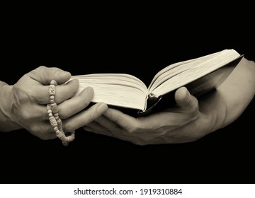 Strong male hands with veins hold a rosary and a book on a black isolated background. Close-up, copy space.