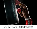 Strong man, boxing athlete intensely training with punching bag, demonstrating strength and determination isolated on black background. Concept of professional sport, active lifestyle, body, strength