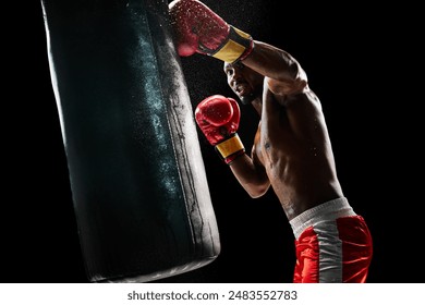 Strong man, boxing athlete intensely training with punching bag, demonstrating strength and determination isolated on black background. Concept of professional sport, active lifestyle, body, strength