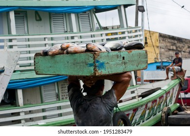 Strong Man Carrying A Big Box Full Of Fish In The Port Of Manaus And A Boat In The Background