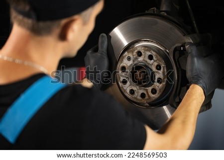 Strong man checks for wear in running gear and steering components. Mechanic at service station checks the brake and steering systems. Service operator in overalls. Car moves on lift.