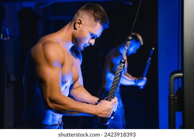 Strong man doing exercise for triceps with rope in the gym